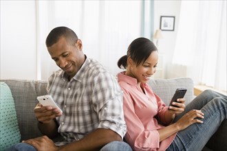 Couple using cell phones back to back on sofa