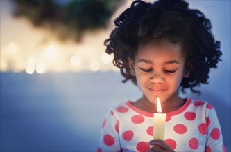 African American girl in pajamas holding lit candle