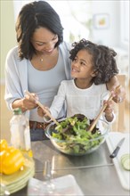 African American mother and daughter tossing salad