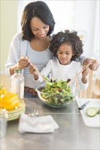 African American mother and daughter tossing salad