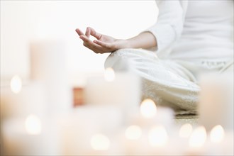 Hispanic woman meditating in lotus position near lit candles