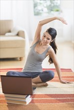 Hispanic woman on rug stretching in front of laptop