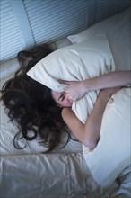 Frustrated Hispanic woman gripping pillow in bed