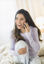 Enthusiastic Hispanic woman talking on cell phone in bed