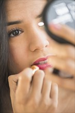 Close up of Hispanic woman applying lipstick in compact mirror