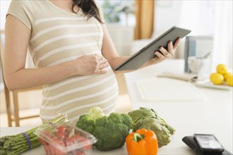 Pregnant Japanese woman using digital tablet in kitchen