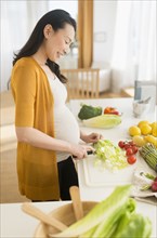 Pregnant Japanese woman slicing vegetables in kitchen