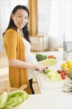 Portrait of pregnant Japanese woman slicing vegetables in kitchen