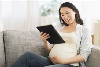 Pregnant Japanese woman using digital tablet on sofa