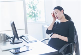 Tired pregnant Japanese businesswoman at desk