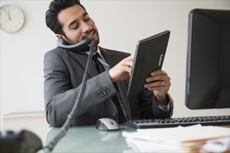 Mixed race businessman using digital tablet on telephone