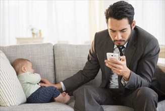 Father sitting with baby and using cell phone