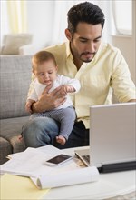 Father holding baby and using laptop