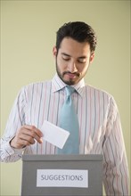 Mixed race businessman placing idea in suggestion box