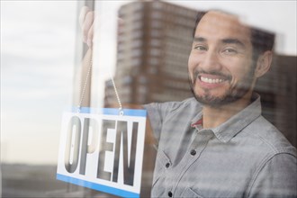 Mixed race man placing Open sign in shop window