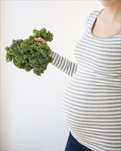 Pregnant Caucasian woman holding head of kale