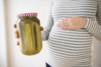 Pregnant Caucasian woman holding jar of pickles