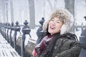 Asian woman sitting on park bench in snow
