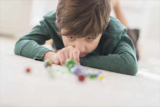 Hispanic boy playing with marbles on bedroom floor
