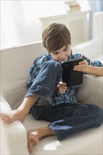 Hispanic boy using digital tablet in armchair