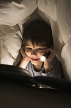 Hispanic boy reading under covers