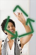 Black woman drawing green recycling symbol on window