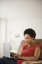 Black woman using laptop in armchair
