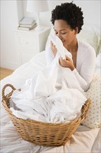Black woman smelling fresh laundry on bed