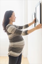 Pregnant Hispanic woman hanging pictures