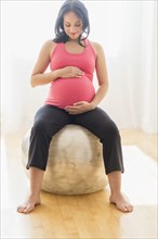 Pregnant Hispanic woman sitting on fitness ball
