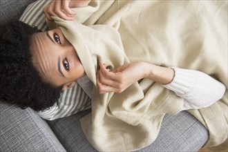Black woman wrapped in blanket on sofa