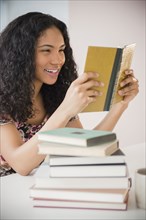 Mixed race woman reading stack of books