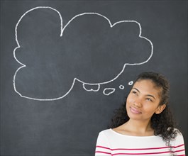 Mixed race woman under thought bubble on chalkboard