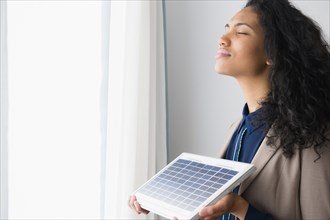 Mixed race woman holding solar panel by window