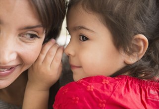 Hispanic girl whispering in mother's ear