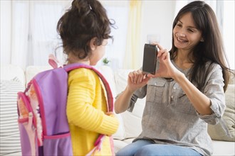 Hispanic mother taking picture of daughter ready for school