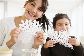 Hispanic mother and daughter making paper snowflakes