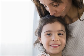 Hispanic mother kissing top of daughter's head