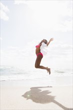 African American woman jumping for joy on beach