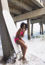 African American woman leaning on surfboard on beach