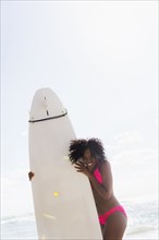 African American woman holding surfboard on beach