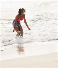 African American woman playing in waves on beach