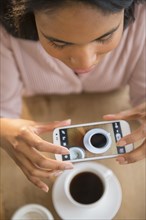 Mixed race woman taking cell phone picture of coffee cup