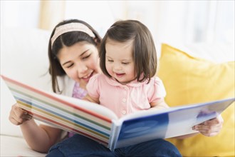 Hispanic girl reading to toddler sister in living room