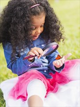 Mixed race girl examining butterfly with magnifying glass