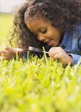Mixed race girl examining grass with magnifying glass