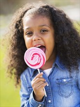 Mixed race girl licking lollipop outdoors