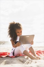 Mixed race girl using digital tablet on beach
