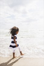 Mixed race girl walking in waves on beach