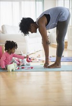 Mother stretching as daughter plays on yoga mat